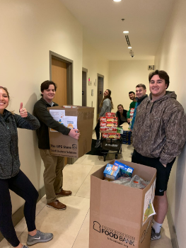 Students pose in a hallway with boxes of food donations.