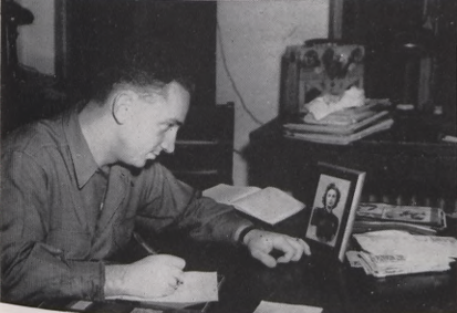 Student writes a letter while looking at photo on desk. 